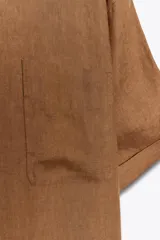Blusa color marrón confeccionada en lino 100%, de corte holgado, cuello redondo, manga corta y bolsillo de parche en el pecho.