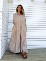 Vestido camisero largo color beige con rayas verticales blancas, cuello camisero, abotonadura frontal completa, mangas largas con puños abotonados y falda con volantes.