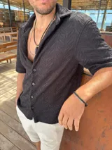 Camisa negra tejida de manga corta con cuello camisero y cierre frontal con botones.