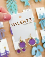 Aros colgantes con forma circular, con centro de color lila y borde con strass plateados. El aro es de acero dorado.