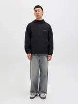 Campera softshell negra con capucha ajustable con cordón, mangas largas con puños de canalé, cierre frontal con cremallera y bolsillos delanteros. Forro sin relleno y costuras cubiertas.