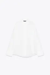 Camisa blanca de algodón, corte amplio, con cuello solapa, manga larga con puños y hombros caídos. Tiene un bolsillo de parche en el pecho, pinzas en la espalda y cierre frontal con botones.