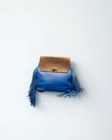 Mochila pequeña de cuero sintético azul con solapa marrón y cierre de giro dorado. Presenta flecos colgando de los laterales.