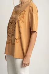 Remera color ocre de corte oversize, con estampado de flores y texto en francés.
