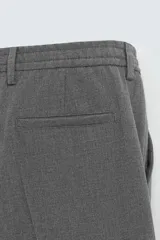 Pantalón negro de corte ancho con cintura elástica, pliegues frontales, bolsillos laterales y traseros de vivo. Tiene detalle de hebilla metálica en la trabilla y cierre frontal con cremallera y botón.