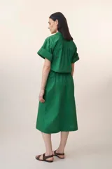 Vestido camisero midi verde esmeralda con cuello camisero, mangas cortas con puños, cierre frontal con botones y cinturón de lazo a juego.