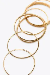 Pack de siete pulseras rígidas metálicas doradas con textura acanalada.