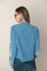 Camisa de jean celeste con bordados de flores blancas en hilo de seda, cuello mao y cierre frontal con botones.