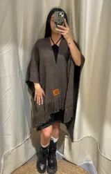 Ruana marrón de lana merino uruguaya con flecos en el ruedo y etiqueta con logo en el frente.