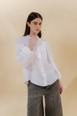 Camisa blanca de lino con cuello mao, mangas largas abullonadas con elástico en los puños, botones forrados en la misma tela y detalle de blonda de algodón en cuello, botones y hombros.