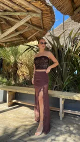 Pollera larga de microtul color marrón, con diseño de transparencias, detalle de fruncido lateral y volados verticales a lo largo de la abertura frontal.