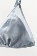 Bralette triangular color gris celeste, confeccionado en seda. Tiene tirantes finos regulables y cierre trasero con gancho metálico.