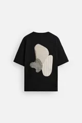 Camiseta negra de corte holgado con cuello redondo y mangas cortas. Estampado frontal con la frase "Unfolding Dreams" en letras blancas.