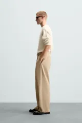 Pantalón negro de corte amplio con cinturón de tela con hebilla metálica. Presenta pliegues frontales, bolsillos laterales y traseros. Cierre frontal con cremallera y botón.