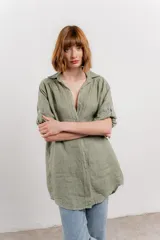 Camisa larga color verde oliva, confeccionada en lino 100%, de corte recto y calce suelto. Presenta cuello camisero, botones en el frente y mangas largas que se pueden arremangar con presilla y botón.