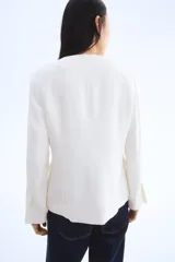 Blazer entallado color blanco con cuello redondo, cierre frontal con un botón visible y tapeta con botones ocultos. Tiene bolsillos delanteros ribeteados, abertura en los puños y pinzas moldeadoras adelante y atrás. Está forrado.
