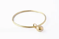 Pulsera dorada tipo brazalete con dije colgante en forma de esfera.