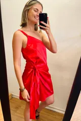 Vestido corto de satén color rojo, con un solo tirante, corte asimétrico, detalle de lazo en la cintura y falda drapeada.