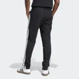 Pantalón de jogging Adidas Essentials con corte clásico, color negro con tres rayas blancas a los costados, cintura elástica con cordón de ajuste, bolsillos frontales y logo bordado.