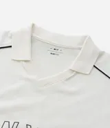 Remera tipo polo de hombre, color blanco crudo, con escote en V ribeteado en negro y ribetes negros en las costuras de los hombros. Presenta la inscripción arqueada "NEW YORK" en negro en el pecho.
