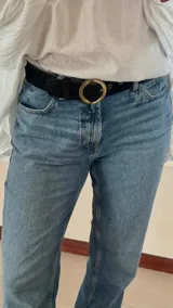 Cinturón negro de cuero con hebilla circular dorada.