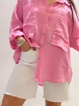 Camisa oversize rosada de lino, con cuello clásico, cierre frontal con botones, dos bolsillos de parche en el pecho y mangas largas con puños abotonados.