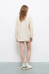 Camisa color crema con rayas verticales finas, de corte holgado y más larga en la parte posterior.
