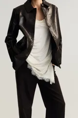 Jean de cinco bolsillos, tiro alto, color marrón oscuro o negro, con piernas anchas y rectas. Presenta cierre frontal con botón y remaches metálicos dorados.