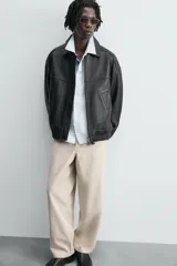 Pantalón chino color beige, de corte relaxed fit, confeccionado en tejido de mezcla de algodón y lino. Cuenta con bolsillos delanteros y traseros de vivo. Cierre frontal con cremallera y botón.