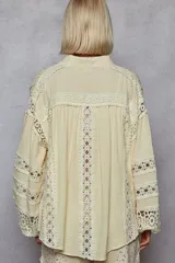 Camisa color crema de corte amplio, con cuello clásico, cierre frontal con botones y mangas largas tipo kimono con detalles de broderie en puños y frente.
