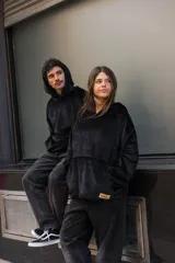 Canguro unisex negro de tela suave con capucha y bolsillo delantero tipo canguro. Tiene cordón ajustable en la cintura para usarlo largo o corto.