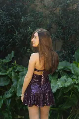 Vestido corto de lentejuelas color ciruela o morado oscuro, con escote corazón y detalle de argolla central que conecta con tirantes finos que atan al cuello. Presenta aberturas laterales (cut-outs) en la zona de la cintura y falda corta con vuelo.