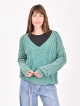 Buzo de tejido de punto color verde menta, con cuello en V y diseño de trenzas en el frente y mangas. Presenta un efecto desgastado o lavado.