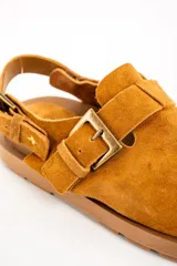 Zueco color camel de gamuza, con suela marrón y dos hebillas ajustables.