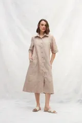 Vestido camisero midi color beige, de lino, con abotonadura frontal completa, manga ranglan, bolsillos laterales y un volante en el ruedo.