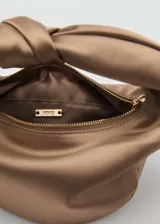 Bolso de mano color beige de tejido satinado con asa superior con nudo decorativo. Tiene cierre de cremallera, forro interior y asa de cadena desmontable.