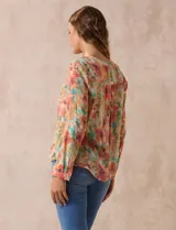 Blusa de gasa estampada a rayas verticales en tonos celeste, lila, naranja y marrón. Tiene cuello a la base con escote en V y botones. Delantera con bolsillo aplicado. Largo de manga regulable con presilla y botón. Terminación anudada opcional.