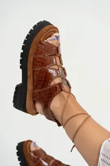 Sandalias de cuero color marrón con textura de cocodrilo, plataforma con suela track y tiras finas que se atan al tobillo.