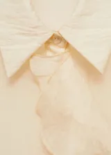 Camisa color crema de corte recto, con cuello camisero, cierre frontal con botones ocultos, manga larga con puños abotonados y detalle de volantes en el frente.