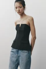 Top negro palabra de honor con escote recto y detalle de pieza metálica en forma de V forrada. Tiene falsos bolsillos con solapa en el delantero, forro interior combinado y cierre lateral con cremallera oculta.