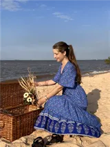 Vestido largo azul con estampado floral, escote en V, botones frontales, mangas cortas con volados y lazo ajustable en la cintura.