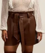 Short de cuero sintético color marrón, de tiro alto, con trabillas en la cintura, pliegues delanteros, bolsillos tipo cuchillo y cinturón para lazo.