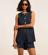 Chaleco femenino confeccionado en jeans, sin mangas, cinturado, con botones y bolsillos. De corte alargado y cuello redondo.