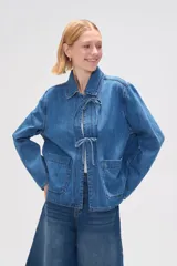 Chaqueta de jean azul con cuello camisero, cierre frontal con lazos y bolsillos de parche.