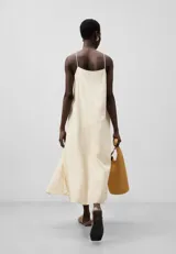 Vestido midi color crema con breteles finos, escote en V y corte asimétrico. Presenta una sección lisa y otra con bordado calado.