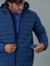 Campera acolchada azul con capucha, cierre frontal con cremallera y bolsillos laterales con cremallera. Diseño ligero y funcional. Marca Calvin Klein.