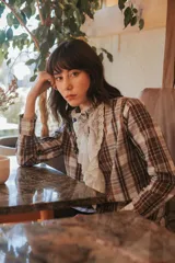 Camisa a cuadros marrón y beige, de algodón con cuello y pechera de tul bordado. Tiene botones de nácar en la cartera y los puños.