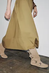 Bota alta color beige de serraje con puntera redondeada. Presenta tres tiras con hebillas metálicas en la parte delantera y caña.
