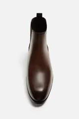 Bota Chelsea de cuero color marrón oscuro, con puntera fina, paneles laterales elásticos y tirador trasero.