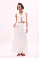 Chaleco blanco, estilo crop top, con escote en V y cierre frontal anudado con cordones.